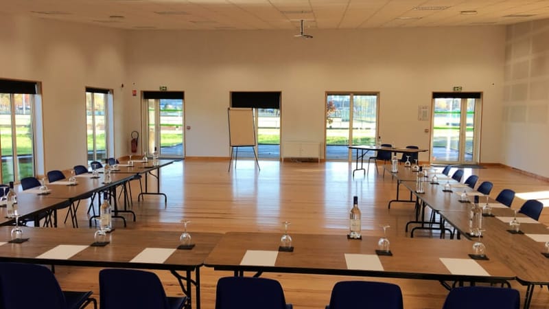 Grande salle de séminaire aménagée avec des tables en U, des chaises bleues et des bouteilles d'eau, à Mérignac