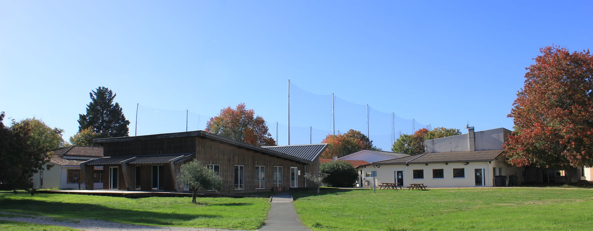Bâtiments en bois et grande pelouse bordée d'arbres d'un domaine sportif, à Mérignac