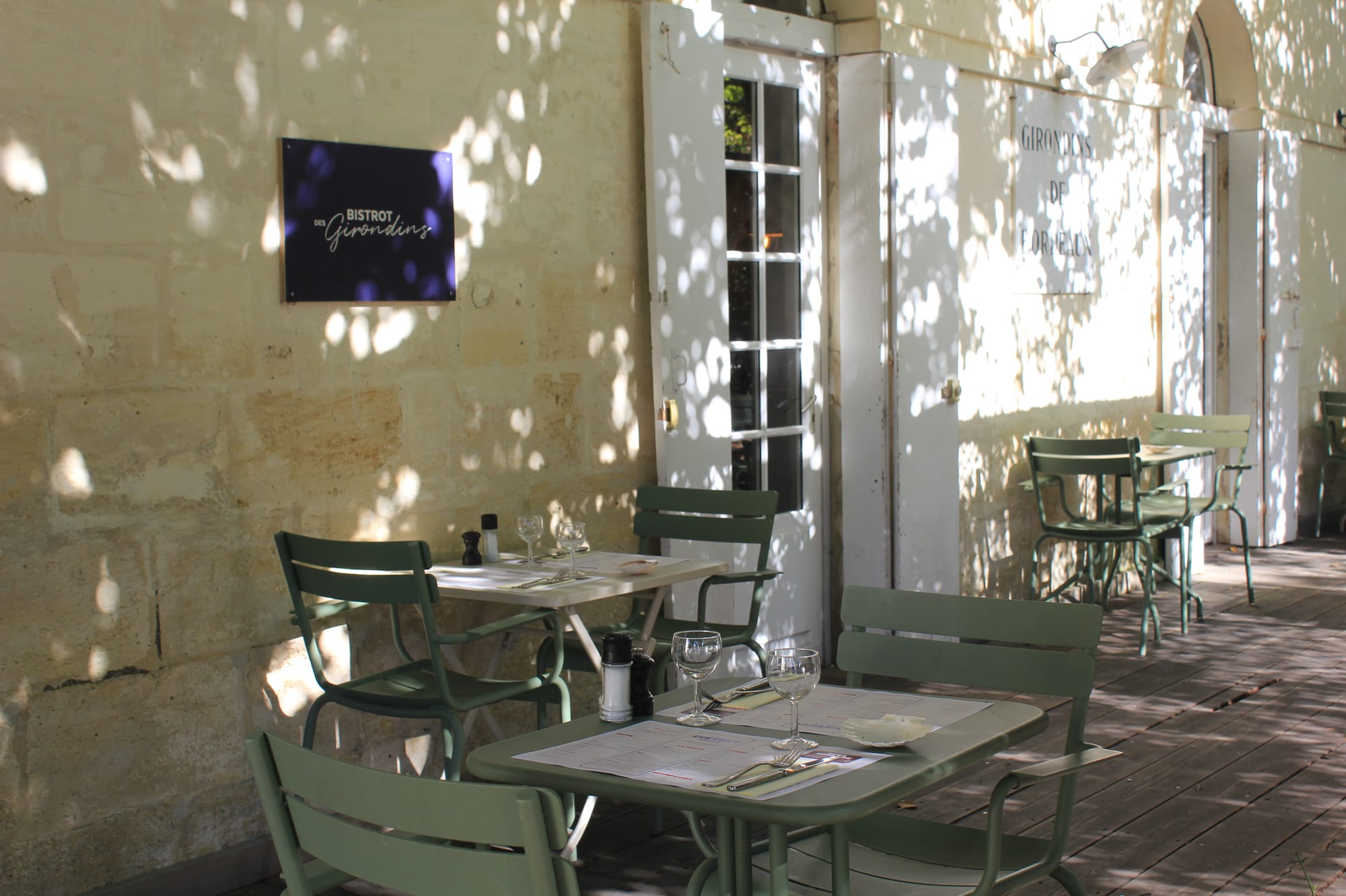 Tables dressées et chaises vertes sur la terrasse ombragée du Bistrot des Girondins, à Mérignac
