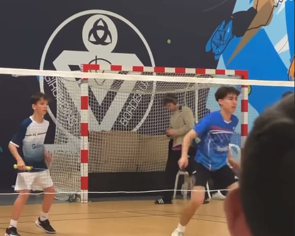 Jeunes joueurs de badminton au filet, devant la fresque du gymnase