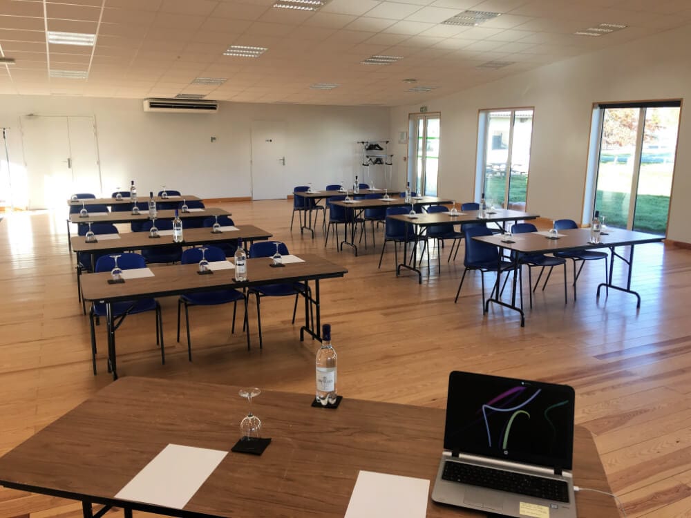 Salle Colloque disposée en classe, tables face à l'écran