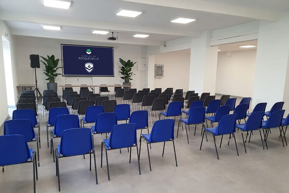 Salle de réception en configuration formation, tables, écran et paperboard
